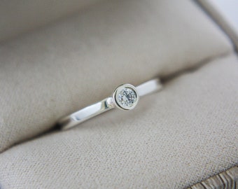 Puede incluir: Un anillo de banda de plata simple con una sola piedra redonda transparente.