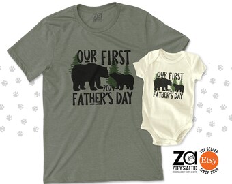 May include: A green t-shirt with the text "Our First Father's Day 2024" and a black bear and cub silhouette. A white onesie with the text "Our First Father's Day" and a black bear and cub silhouette.