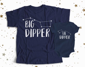 May include: A navy blue t-shirt with the text "BIG DIPPER" and a constellation graphic. A matching navy blue baby onesie with the text "Lil DIPPER" and a constellation graphic.