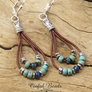 May include: A pair of dangle earrings with brown leather cords and turquoise blue and silver beads. The earrings have silver hooks and a silver bead at the top of each cord.