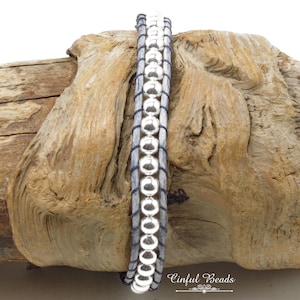 K&ouml;nnte beinhalten: Ein silbernes Perlenarmband mit einem grauen Lederband. Das Armband ist um ein St&uuml;ck Treibholz gewickelt. Der Text "Cinflul Beads" ist in der unteren rechten Ecke des Bildes sichtbar.