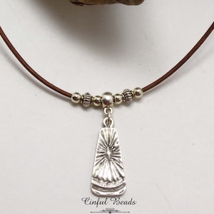 May include: A silver pendant necklace with a starburst design hangs from a brown leather cord. The cord is accented with silver beads.