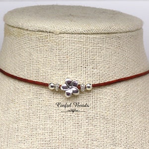 May include: A brown leather choker necklace with a silver flower charm and silver beads.