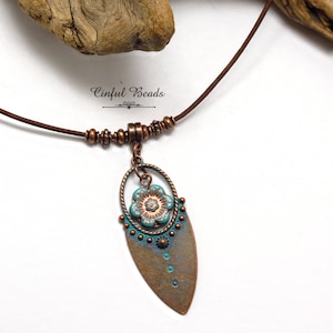 May include: A copper necklace with a turquoise and copper pendant featuring a flower design. The necklace is made with a brown leather cord and has a copper clasp.