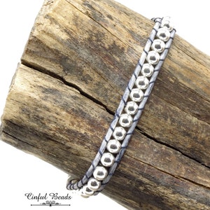 K&ouml;nnte beinhalten: Ein graues Lederarmband mit silbernen Perlen. Das Armband ist um ein St&uuml;ck Treibholz gewickelt. Der Text "Cinflul Beads" ist am unteren Rand des Bildes sichtbar.