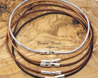 May include: Four leather cord necklaces with silver clasps. The cords are in the colors brown, tan, black, and white. The necklaces are displayed on a wooden surface.  Cinfu Beads.