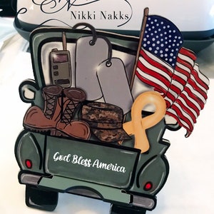 May include: A green toy pickup truck with a white "God Bless America" inscription on the back. The truck is filled with military-themed items, including dog tags, boots, a camouflage hat, and an American flag.