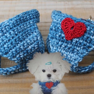 May include: Two blue and white crocheted dog harnesses with red heart accents. One harness has a red heart on the front and the other has a red heart on the back.