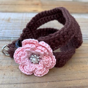 May include: A brown crochet pet collar with a pink crochet flower. The flower has a silver rhinestone center with a pearl. The collar has a silver metal clasp.