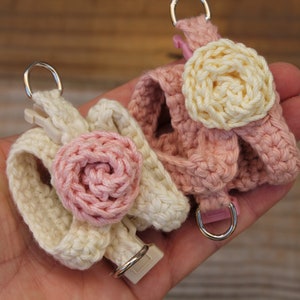 May include: Two crocheted dog harnesses with flower accents. One harness is cream with a pink flower, the other is pink with a cream flower.