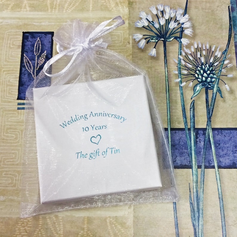 May include: A white gift box with a blue and white design. The box says "Wedding Anniversary 10 Years The gift of Tin". The box is in a white organza bag.
