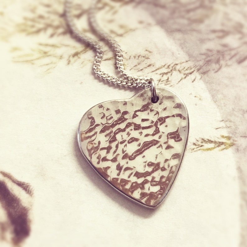 May include: A silver heart-shaped pendant necklace with a textured surface. The pendant is hanging on a silver chain.