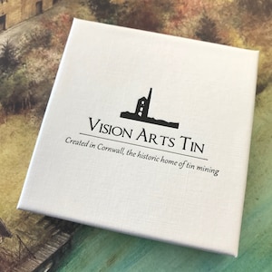 May include: White box with black text and a silhouette of a building. The text reads "Vision Arts Tin" and "Created in Cornwall, the historic home of tin mining."