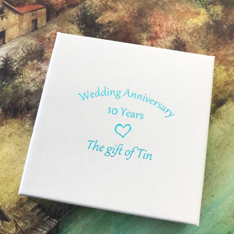May include: White box with blue text that reads "Wedding Anniversary 10 Years" with a blue heart symbol and "The gift of Tin".