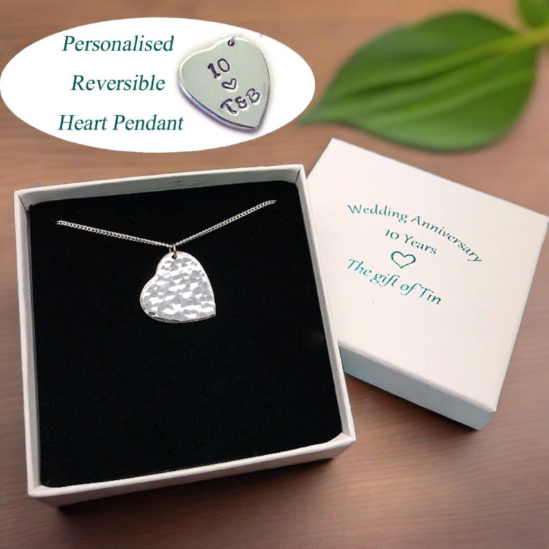 May include: A silver heart pendant necklace in a white box with a black interior. The pendant is textured and has a hammered finish. The box has a label that says "Wedding Anniversary 10 Years The gift of Tin".