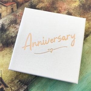 May include: White gift box with the word "Anniversary" written in gold script with a small heart symbol.