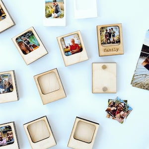 May include: Wooden photo frame magnets with pictures of people. Some frames have photos inserted, others are empty. One frame has the word "family" engraved on it. The frames are made of light-colored wood and have a rectangular shape.