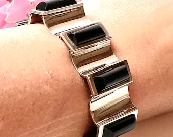 May include: A silver bracelet with black rectangular stones. The bracelet is made of a series of interlocking links, each with a black stone set in the center.