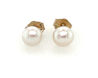 Puede incluir: Un par de pendientes de oro con forma de botón, cada uno con una perla redonda de color blanquecino. Los pendientes tienen un diseño clásico, con un poste y un cierre para un uso seguro. Las perlas tienen un brillo sutil.