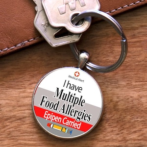 May include: A silver keychain with a round tag that says "Medical Alert I have Multiple Food Allergies Epipen Carried". The tag has a red, white, and gray design with a small red cross and a drawing of an epipen.
