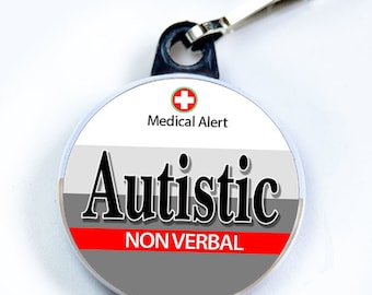 Puede incluir: Una etiqueta de alerta médica redonda y blanca con una cruz roja y el texto "Medical Alert". La etiqueta también tiene una franja gris con la palabra "Autistic" en negro y una franja roja con el texto "NON VERBAL" en negro.