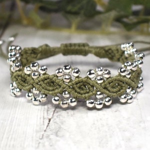 May include: A green braided bracelet with silver beads in a flower pattern.