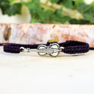 May include: A dark purple braided bracelet with a silver violin charm.
