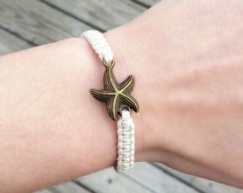 Puede incluir: Pulsera trenzada blanca con un dije de estrella de mar dorada.