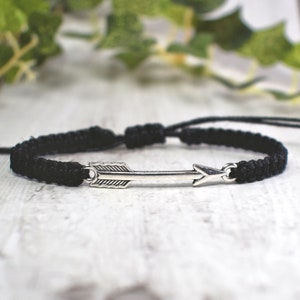 May include: A black braided bracelet with a silver arrow charm.