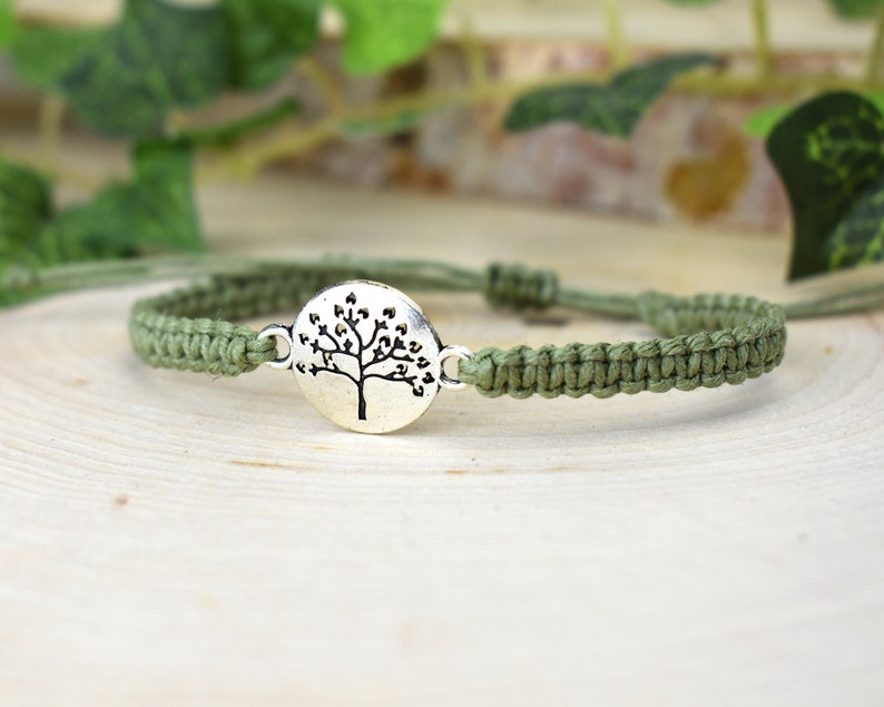 May include: A green braided bracelet with a silver charm featuring a tree of life design.