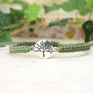 May include: A green braided bracelet with a silver charm featuring a tree with heart-shaped leaves.