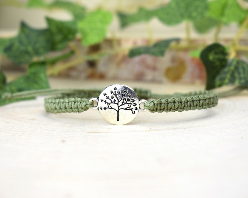 May include: A green braided bracelet with a silver charm featuring a tree with heart-shaped leaves.