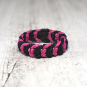 Könnte beinhalten: Ein geflochtenes Armband in Schwarz und Pink aus Kordel.