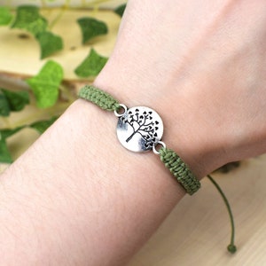 May include: A green braided bracelet with a silver charm featuring a tree design.