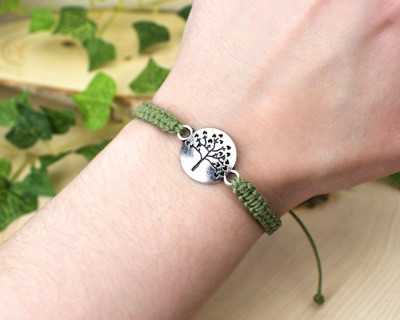 May include: A green braided bracelet with a silver charm featuring a tree design.