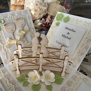 May include: Wedding-themed greeting cards with a bridge and couple silhouette. The cards feature decorative elements like wine glasses, bows, leaves, and the names "Monika & Michal" with "Gratulacje!" text. The cards are white with beige accents.