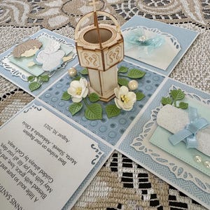 May include: A handmade baptism card with a wooden baptismal font centerpiece, surrounded by light blue and white decorative elements. The card includes text with well wishes and the date August 30, 2025.