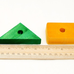 Puede incluir: Cuatro bloques de madera de diferentes formas y colores: un cuadrado rojo, un tri&aacute;ngulo verde, un rect&aacute;ngulo amarillo y un cubo azul. Cada bloque tiene un agujero en el centro.