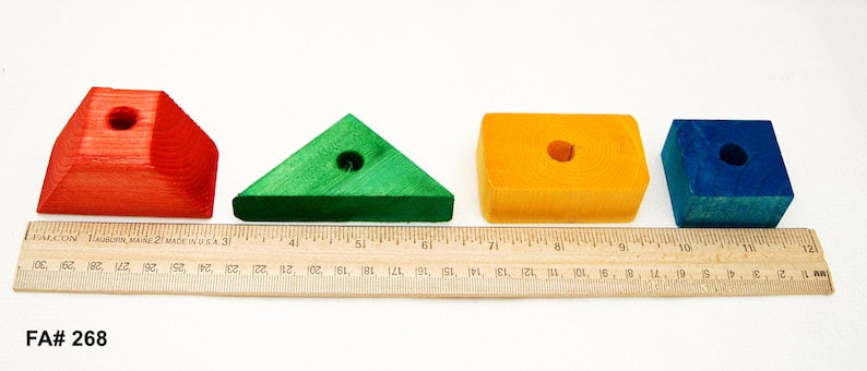 Puede incluir: Cuatro bloques de madera de diferentes formas y colores: un cuadrado rojo, un tri&aacute;ngulo verde, un rect&aacute;ngulo amarillo y un cubo azul. Cada bloque tiene un agujero en el centro.