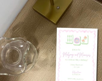 Puede incluir: Una tarjeta de invitación rosa y verde con un borde blanco. La tarjeta presenta un gráfico de tres fichas de mahjong con flores y un círculo. El texto en la tarjeta dice "Join us for Mahjong and Mimagas to celebrate Riky's Birthday! Friday, March 24th 6:30 pm Riky's House 123 Lane Dr RSVP to Riky's email address"