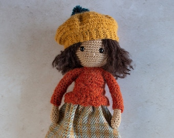 May include: A crocheted doll wearing a yellow beret, an orange sweater, a plaid skirt, and blue shoes.