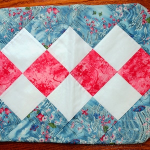 Puede incluir: Un camino de mesa azul y blanco con un patrón de diamantes rosa y blanco. El camino de mesa está hecho de tela con estampado floral.