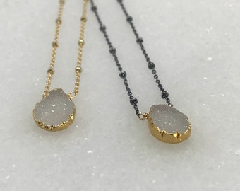 May include: Two delicate necklaces with a white, crystal-like pendant. One necklace has a gold chain and the other has a black chain.