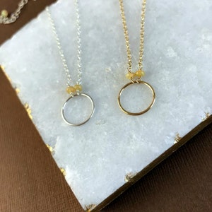 May include: Two delicate necklaces with small, round, yellow opal beads and a simple circle pendant. One necklace is silver and the other is gold.