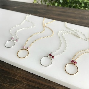 May include: Four delicate necklaces with circle pendants and small gemstone accents. The necklaces are silver, gold, and silver with red and pink gemstones.
