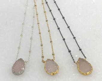 May include: Three delicate necklaces with a teardrop-shaped pink crystal pendant. The necklaces feature silver, gold, and black chain styles.