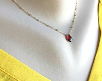 May include: A delicate gold chain necklace with a small, teardrop-shaped red gemstone pendant.