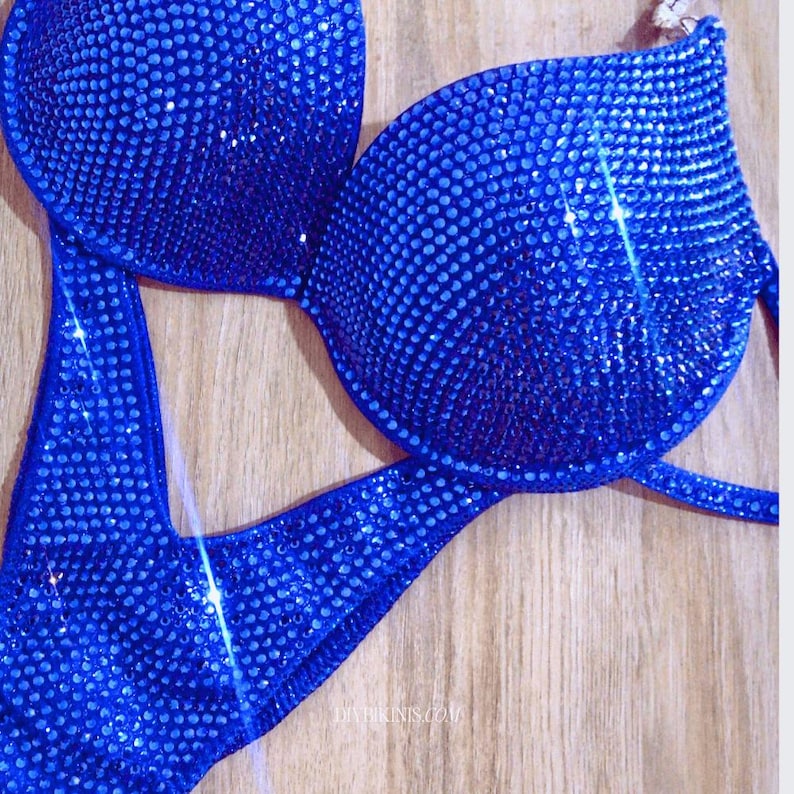 May include: A royal blue bikini with a halter top and a high-cut bottom. The bikini is completely covered in rhinestones.