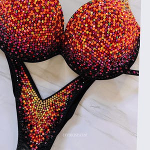 May include: Black bikini with a V-shaped bottom and a halter top. Both pieces are covered in colorful rhinestones, creating a gradient effect from dark to light.