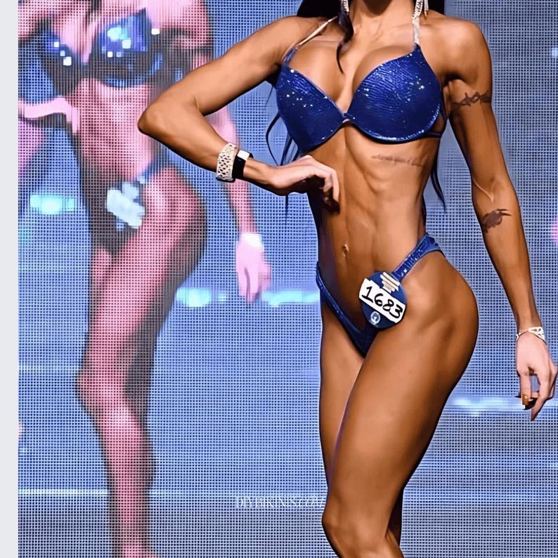 May include: A woman wearing a blue sparkly bikini with a number 1623 on her left hip. She is posing on a stage with a blue and white grid pattern background.